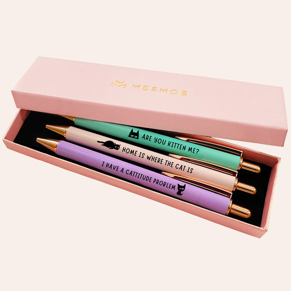 Three pastel pens with cat illustrations in an open pink Mesmos gift box, engraved Are You Kitten Me, Home Is Where The Cat Is and I Have A Cattitude Problem.