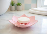 A pink lotus-shaped shower steamer tray holding a round steamer on a bathroom counter.