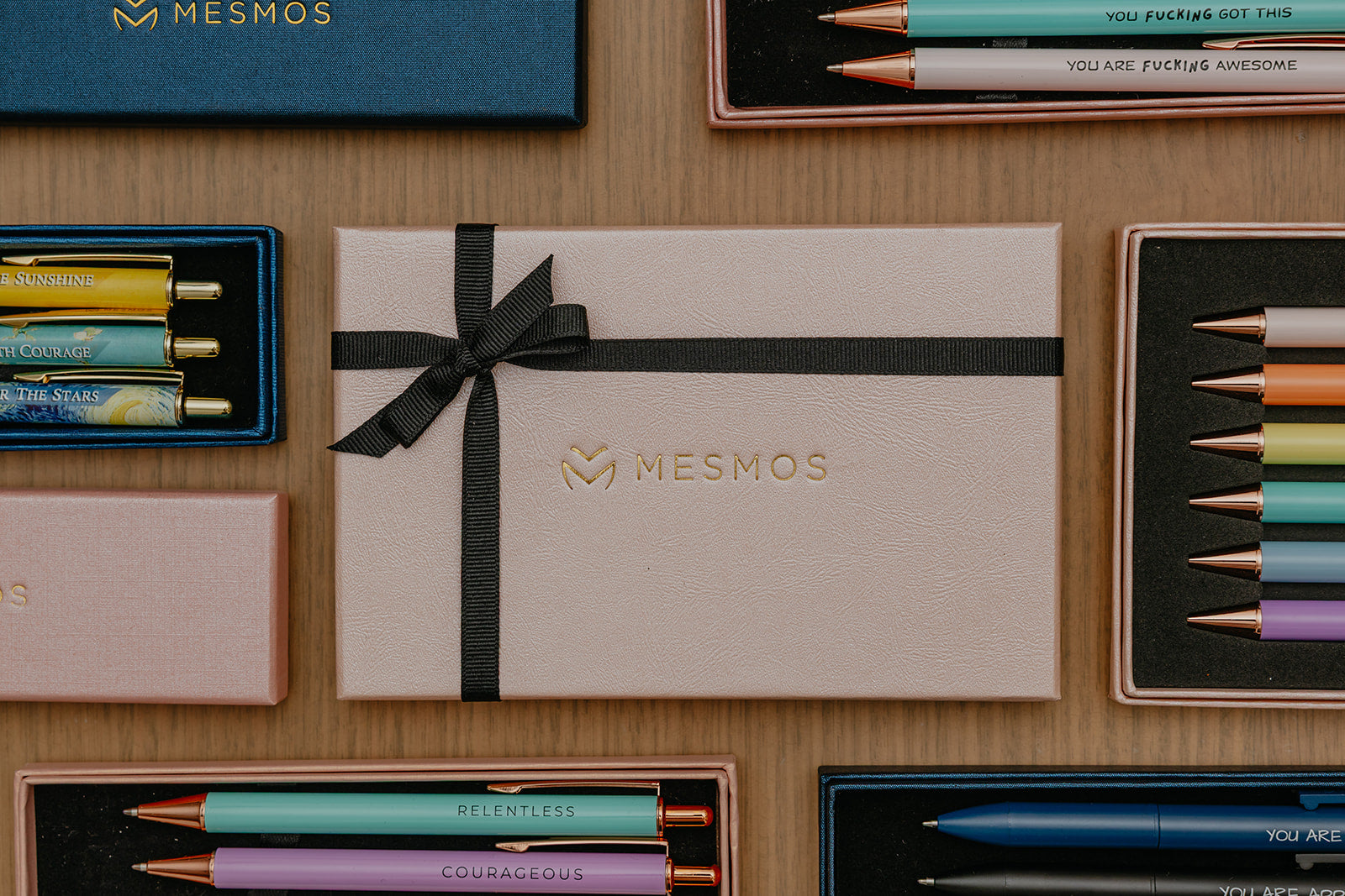 MESMOS branded stationery items including pencils and a box on a wooden surface.