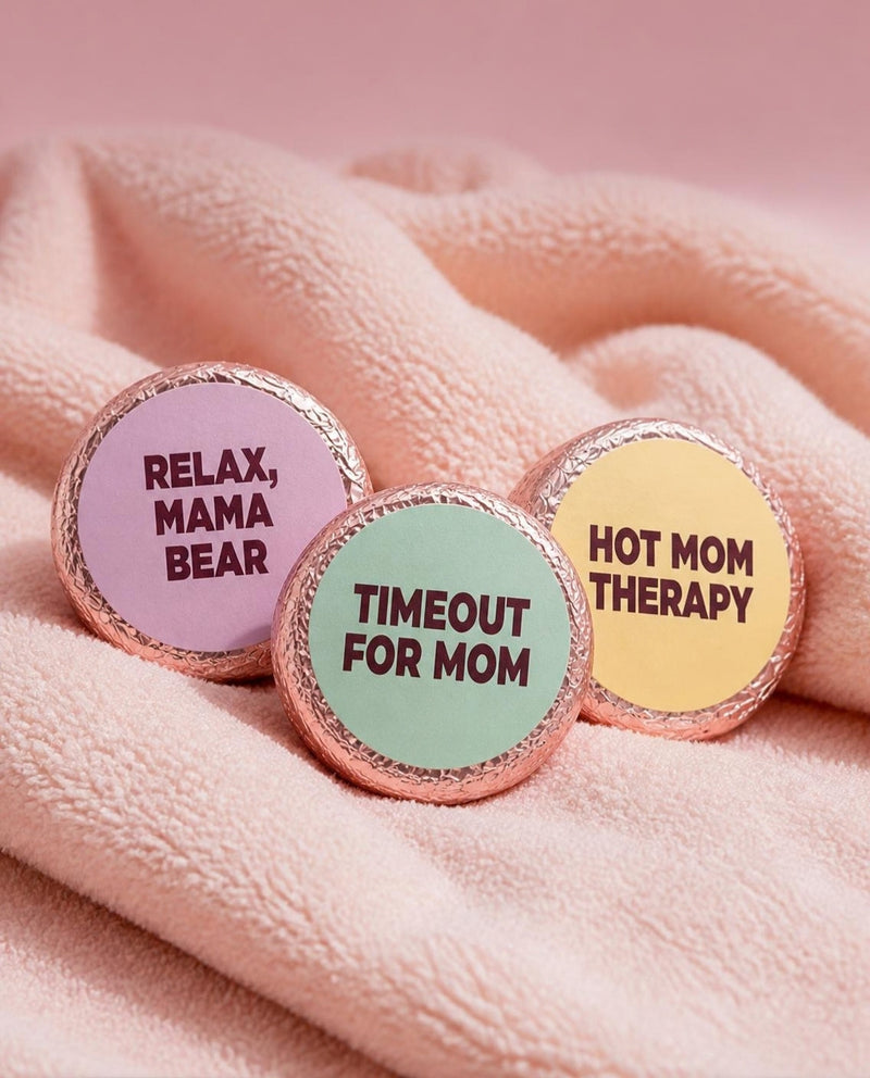 Close-up of three Mesmos Mom Series shower steamers on a pink towel, labelled Relax, Mama Bear, Timeout For Mom and Hot Mom Therapy